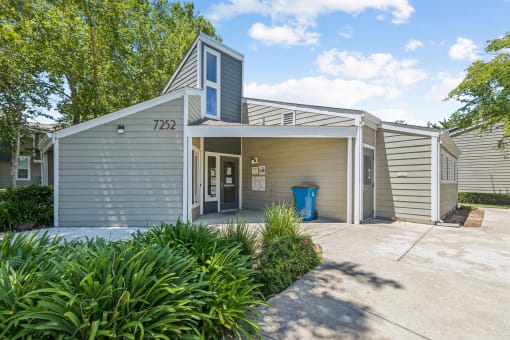 the front of a gray house with a driveway and a blue trash can