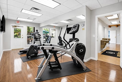 A gym with a row of exercise bikes and a television mounted on the wall.