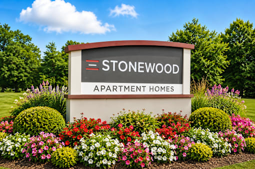 A sign for Stonewood Apartment Homes is surrounded by flowers.