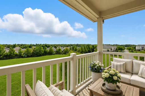 A white couch with pillows is on a wooden porch with a table in front of it.