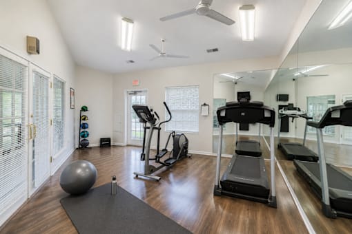 A gym with treadmills, elliptical machines, and a ball on the floor.