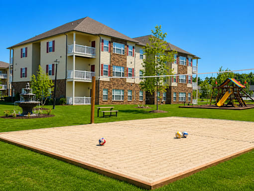 A sandpit in the middle of a grassy area in front of apartment buildings.