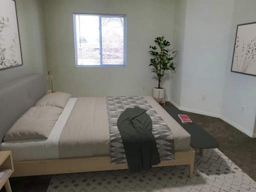 A bedroom with a bed, a small plant, and a painting on the wall.