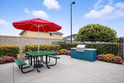 A red umbrella is on a green picnic table.