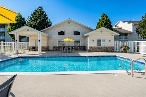 A swimming pool in front of a house with a yellow umbrella.