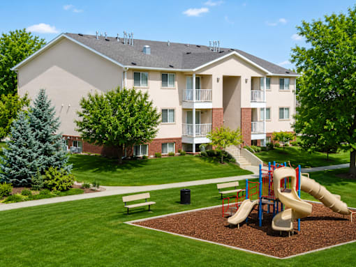 A playground with a slide and a bench in front of a building.