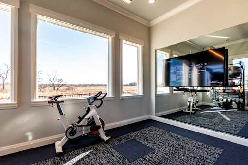 A room with a stationary bike and a TV showing a gym workout.