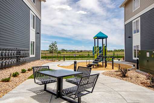 A playground with a blue and yellow tower and a table and chairs in the foreground.