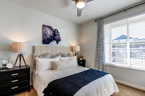A bedroom with a large bed, a ceiling fan, and a painting of a bison head on the wall.