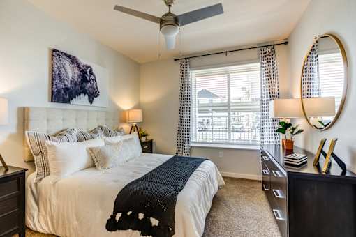 A bedroom with a large bed, a painting of a bison, and a ceiling fan.
