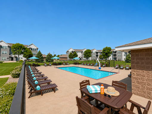 Outdoor swimming pool with lounge chairs and umbrellas at Cypress Court Apartments, St Cloud, 56303