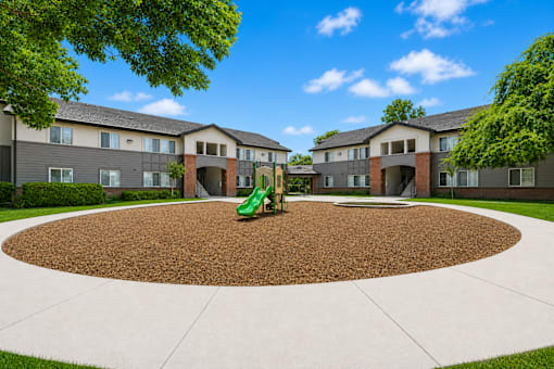 A playground with a green slide in the middle of a courtyard surrounded by apartment buildings.