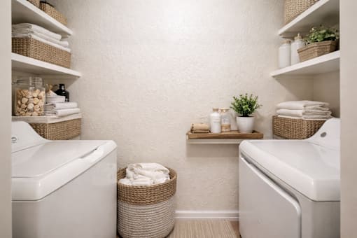 A bathroom with two sinks, a toilet, and a shelf with towels and plants.