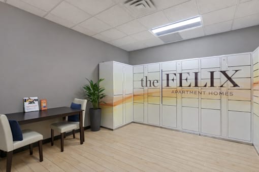 A room with a desk, chairs and a plant, with a wall that has a sign that says