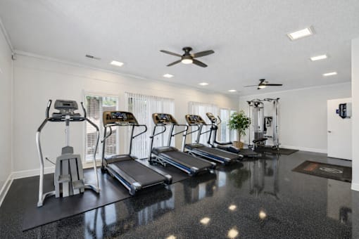 A spacious home gym with treadmills, elliptical machines, and a fan.