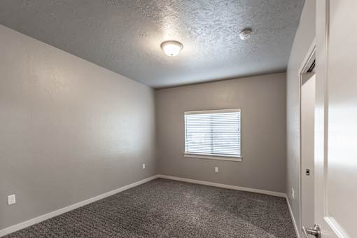 A room with a carpeted floor and a window with blinds.