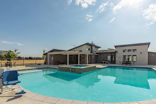 A swimming pool in front of a house with a sunny sky.