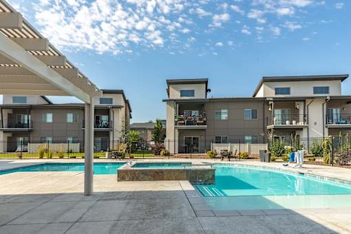 A swimming pool is surrounded by a concrete patio and a building with a balcony.