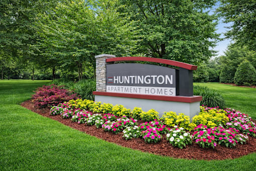 A sign for Huntington Apartment Homes is surrounded by flowers.