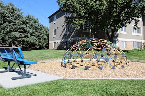 a playground in a yard in front of a house with a tree and a chair