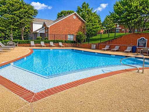 A pool surrounded by a brick border and lounge chairs.