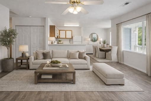 A modern living room with a white sofa set, a wooden coffee table, and a large mirror on the wall.