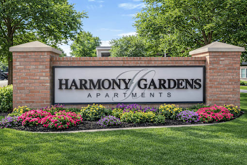 A sign for Harmony Gardens Apartments is framed by flowers and topped by two pillars.