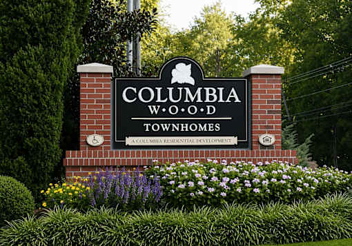 A sign for Columbia W.O.D. Townhomes is displayed in front of a green hedge.