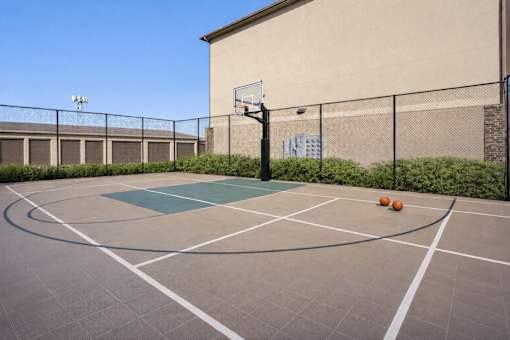 A basketball court with a basketball hoop and two balls on the ground.