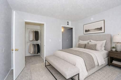 A bedroom with a bed, nightstand, and a closet with clothes.