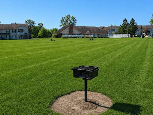 A black trash bin sits on a mound of dirt in the middle of a grassy field.