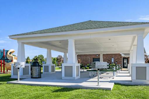 A white pavilion with a green roof is surrounded by a grassy area.