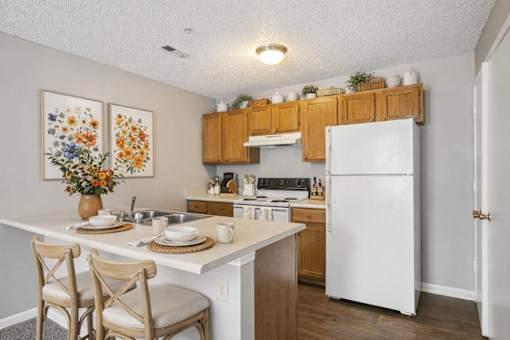 A kitchen with a white fridge, wooden cabinets, and a table with chairs.