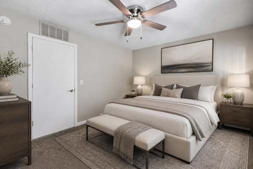 A bedroom with a large bed, a bench, and a ceiling fan.