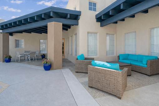 Covered patio with wicker furniture and bright blue cushions at Vista Linda Apartments, Santa Fe, NM 87507