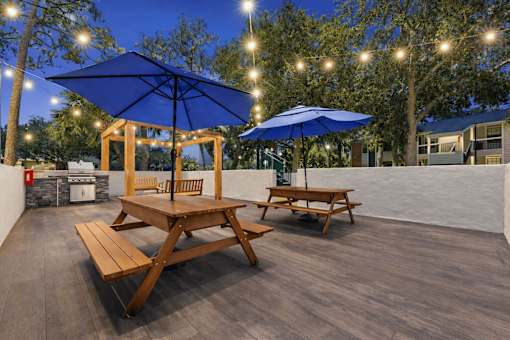 A wooden picnic table with a blue umbrella is set up on a wooden deck. at Epic Apartments , Daytona Beach, FL, 32114