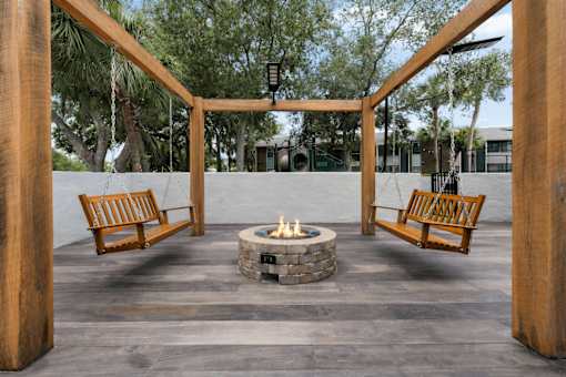 A fire pit is surrounded by two wooden benches and a wooden pergola at Epic Apartments , Daytona Beach
