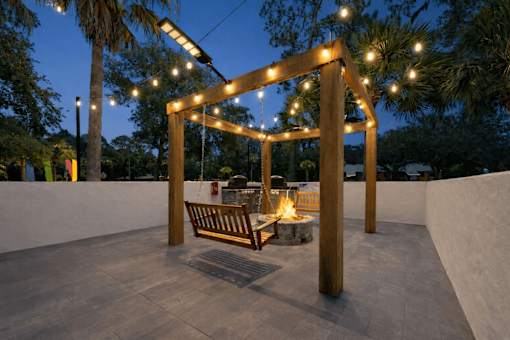 A wooden pergola with lights and a bench is set up in a courtyard. at Epic Apartments , Apartments, Daytona Beach, FL