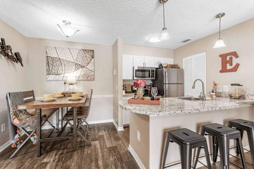 A kitchen with a table and chairs in the foreground and a refrigerator with a letter E on it in the background. at Epic Apartments , Daytona Beach, FL, 32114