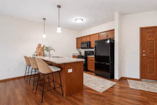 Kitchen with island seating and black appliances at The Estates at Arbor Oaks Apartments, Andover, MN 55304