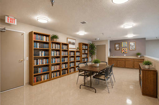 A room with a long bookshelf and a table with chairs.