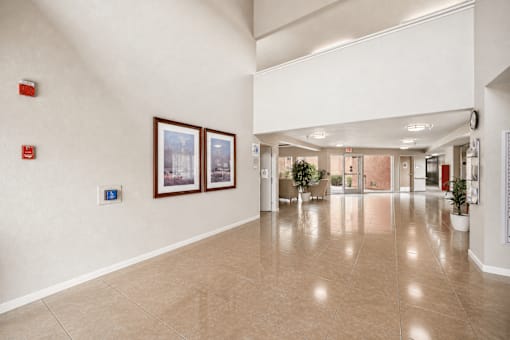 A hallway with a tiled floor and white walls, with two framed pictures on the wall.