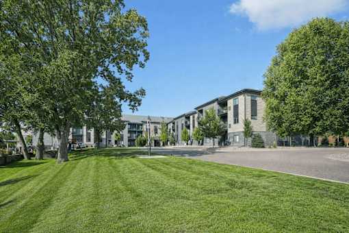 A grassy area in front of a building with trees on the sides at Aster Meadow, Vadnais Heights, MN, 55127