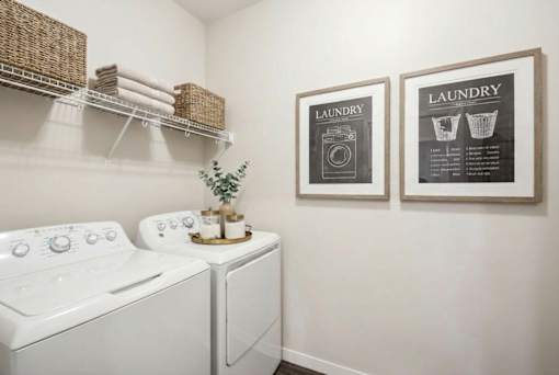 A laundry room with a washer and dryer, a shelf with baskets, and two framed laundry instructions at Aster Meadow, Vadnais Heights, MN, 55127