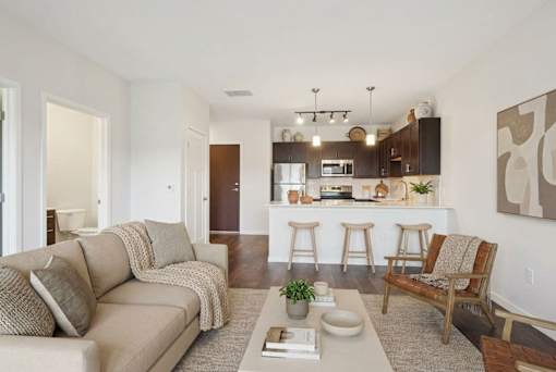 A living room with a couch, a chair, a coffee table, and a kitchen area in the background at Aster Meadow, Vadnais Heights, MN, 55127