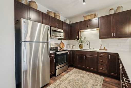 A kitchen with a stainless steel refrigerator and wooden cabinets at Aster Meadow, Vadnais Heights, MN, 55127