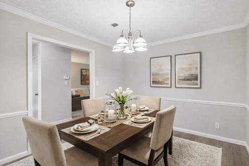 A dining room with a table set for two and a chandelier hanging from the ceiling.