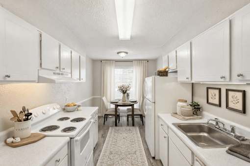 A white kitchen with a stove, sink, and dining table.