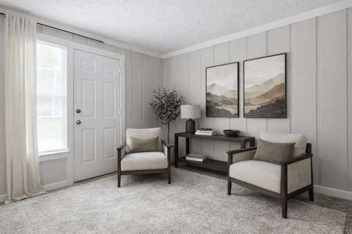 A living room with a white door, two chairs, a table, and two pictures on the wall.