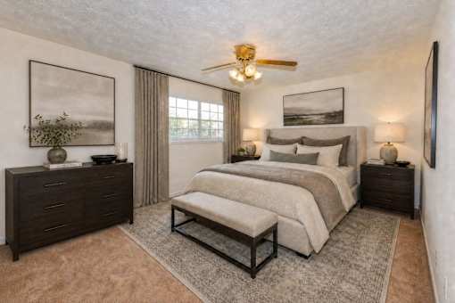 A bedroom with a large bed, a bench, and a ceiling fan.